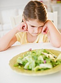 Upset Girl ( 6-7) sitting at table with salad meal