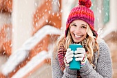 Junge Frau in Winterkleidung trinkt aus einem Thermobecher