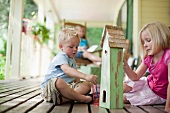 Brother and sister painting birdhouse together