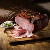 Smoked baked ham, partly sliced, with bread, pickled gherkins and pearl onions