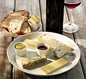 A plate of cheese with mustard, bread, butter and wine