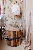 White lamp on bedside table made from bundled logs and round glass top