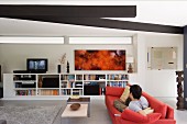 Young man on a red sofa with a view of a TV on the entertainment unit