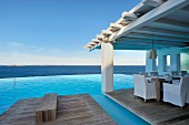 Infinity pool and seating area on roofed wooden deck with sea view