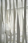 View through ribbons hanging from wooden frame of four-poster bed with white bedlinen