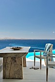 Rustic table and white wicker chairs on terrace next to pool with view of sea