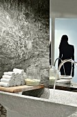 Stone trough and towels on vintage wooden board against stone wall with silhouette motif of woman on glass door