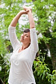 Women with stretching with arms overhead in the garden
