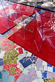 Stühle aus transparentem Kunststoff auf rotem Teppichläufer und mosaikartig gestaltetem Fussboden