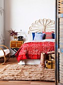 Double bed with headboard shaped like a peacock fan, colourful scatter cushions and bedspread with ethnic pattern; tall leather boots on fur rug in foreground