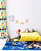 Child's bed below aeroplane silhouettes and colourful clock on wall next to retro curtain with pattern of coloured circles