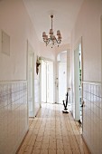 Elegant, narrow hallway with chandelier, half-height tiled walls and rustic wooden floor