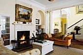 Verschiedene, traditionelle Polstermöbel vor brennendem Kaminfeuer in englischem Herrenhaus