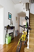 Folding bike at foot of stairs in hall of London house with collection of pictures on wall