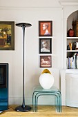Designer standard lamp and nest of plexiglass tables below collection of paintings on wall