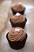 Three chocolate cupcakes with pink sugar flowers