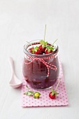 Jar of wild strawberry jam with spoon on white background