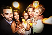 Smiling young people photograph themselves holding cocktails