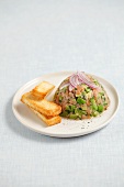 Smoked salmon and avocado tartar topped with onions and served with toast