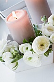 White ranunculus and lit candle in white dish