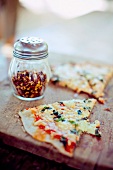 A Slice of Thin Crust Pizza with a Shaker of Red Pepper Flakes
