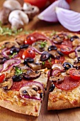 Pizza mit Peperoniwurst, Oliven, Tomaten, Champignons und Zwiebeln, angeschnitten