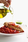 Olive oil being drizzled over a chicken breast on a bed of beetroot couscous