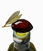 A black olive on top of an olive oil bottle