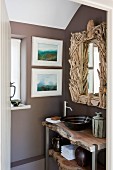 Rustic washstand under bathroom mirror with artistic driftwood frame; two modern watercolour landscapes on wall to one side