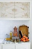 Plate of fruit and Moroccan tea glasses on marble worksurface of kitchen counter in front of tiled splashback below wall units with Oriental pattern on doors