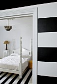 Black and white striped wall and view through open door of bed with white-painted wooden frame on black and white striped rug