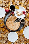 An apple pie and a mug of coffee surrounded by autumn leaves