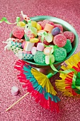 green ice cream dish with sweets, candles, green party streamers and two paper drinks umbrellas on pink glittery background