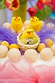 still life arrangement of Easter simnel cake with pink chiffon ribbon and yellow chicks with spring tulips