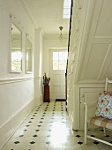 Flur mit Fliesenboden, weiss lackierter Holztreppe, weissen Wänden und Wandspiegeln