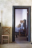 Schlichter Holzstuhl an tapezierter Wand mit strahlenförmigen Motiven neben offener Tür zum Schlafzimmer