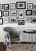 Wicker chair against white wooden wall with large collection of black-framed photographs