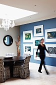 Modern artworks on blue wall; round dining table and chairs with patterned loose covers below large skylight