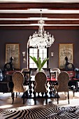 Modern African art and huge vase of leaves in palatial dining room with zebra-skin rug and crystal chandelier