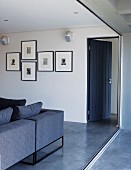 Offene, blaue Holztür mit Wohnzimmercouch im selben Farbton und einer Sammlung Tuschezeichnungen an der Wand vom Balkon aus gesehen