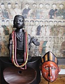 Necklaces hanging on African wooden figurine on polished wooden ornament and wooden mask in front of Chinese picture on wall