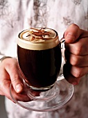 Hands holding a glass mug of Irish coffee