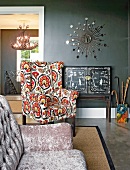 Eclectic mixture of styles with black, Chinese-style cabinet, sunburst mirror and reading chair with cheerful upholstery; couch with iridescent velvet cover in foreground