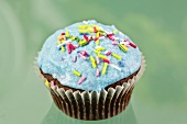 A chocolate cupcake decorated with blue buttercream icing and sugar strands