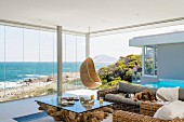 Life by the sea; living room with rustic coffee table, wicker furniture and magnificent view of sea and coast