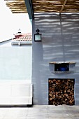 Firewood stacked in square niche shaded by bamboo roof