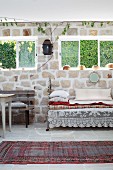 Traditional runner on floor in front of vintage daybed with cushions below windows in stone wall