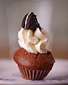A chocolate cupcake topped with cream and a chocolate biscuit
