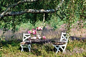 Gedeckter Gartentisch mit Napfkuchen und Sommerblumen unter einer Birke