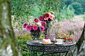 A garden table laid with Bundt cake, teacup, summer flowers and a hurricane lamp